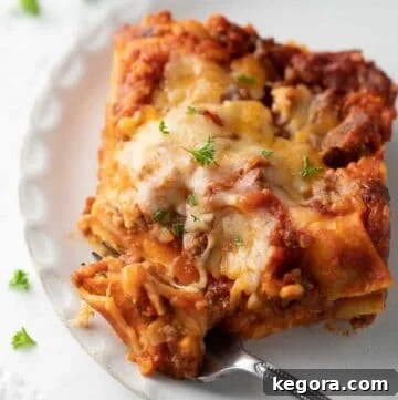 A perfectly portioned slice of gluten-free lasagna on a white plate with a fork, garnished with fresh parsley.