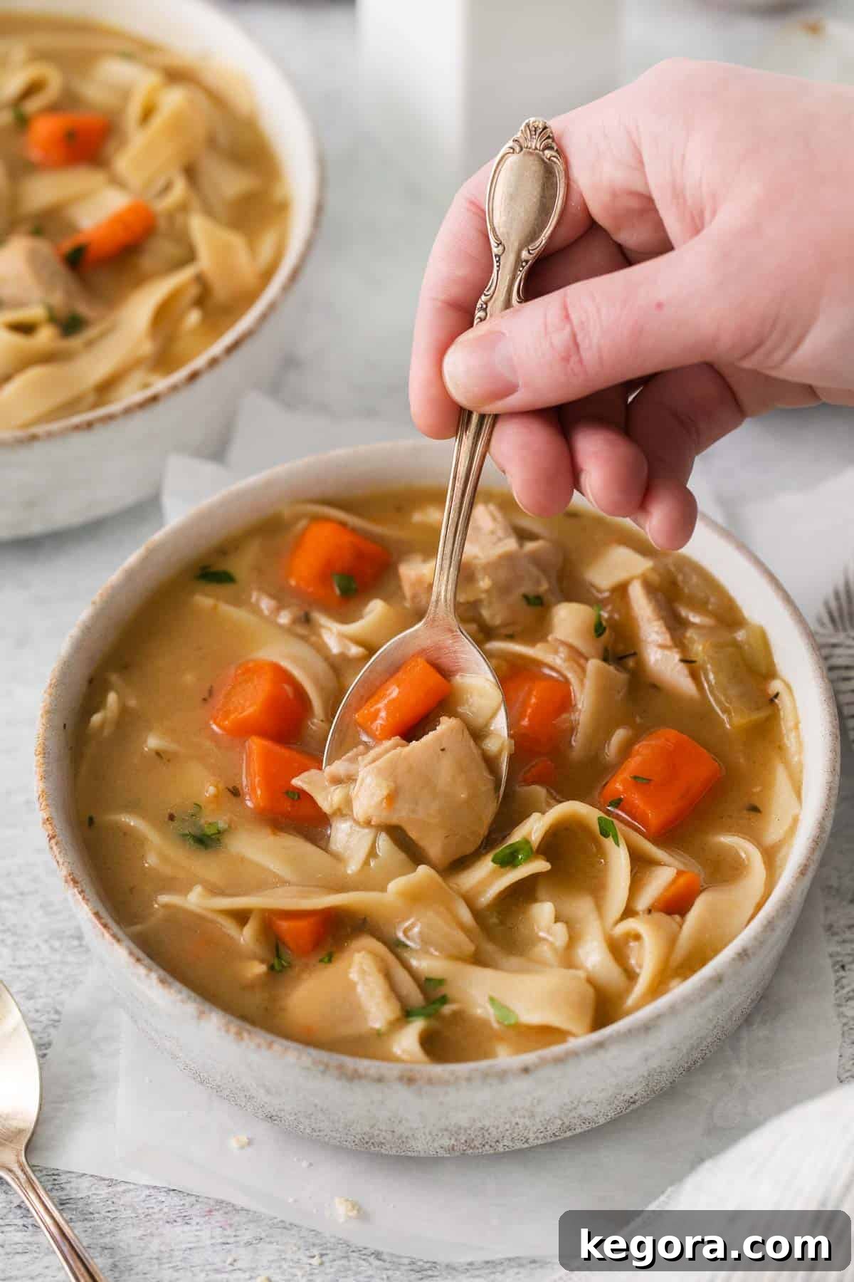 Soul-Soothing Gluten-Free Chicken Noodle Soup 6 A bowl of gluten-free chicken noodle soup, with a hand holding a spoon