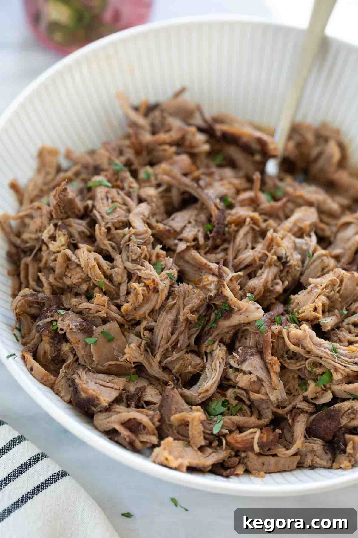 Fork-Tender Sweet Pork Tacos 9 shredded pork tenderloin in white bowl topped with cilantro on marble background