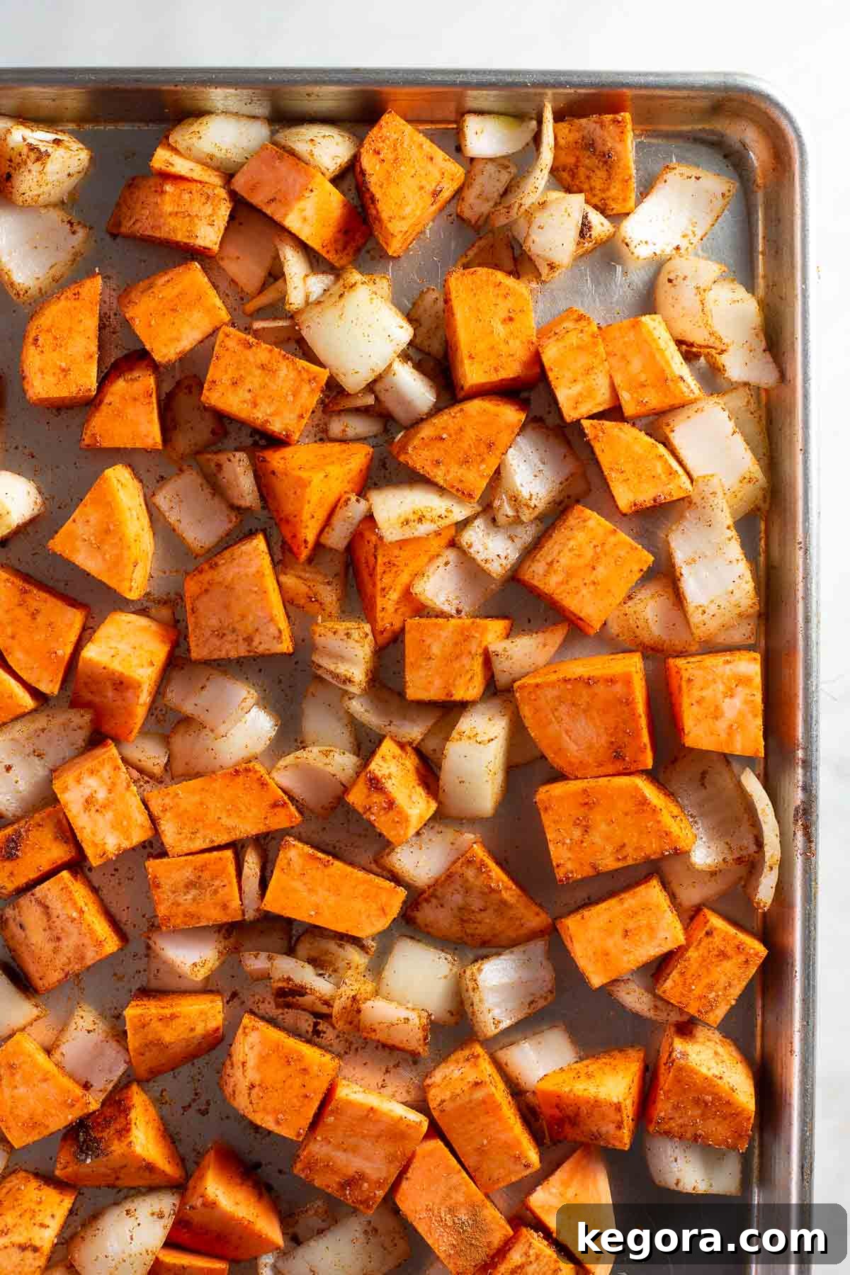 Fresh Ingredients for Roasted Sweet Potato Soup Close-up of cubed raw sweet potatoes and chopped sweet onion on a baking sheet, glistening with olive oil and spices, ready for the oven.
