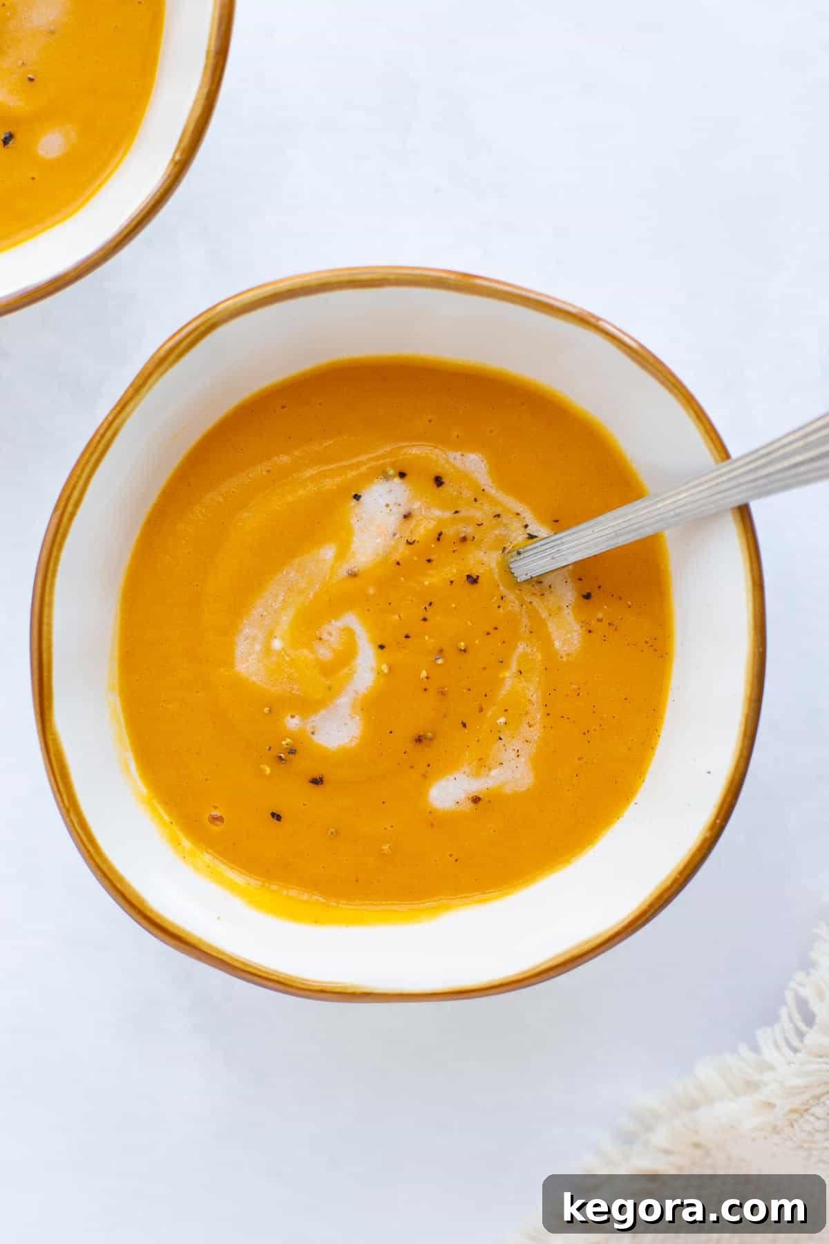 Enjoying Roasted Sweet Potato Soup A spoon dipping into a cozy white bowl of creamy roasted sweet potato soup, garnished lightly with fresh herbs or a drizzle of cream, inviting a taste.