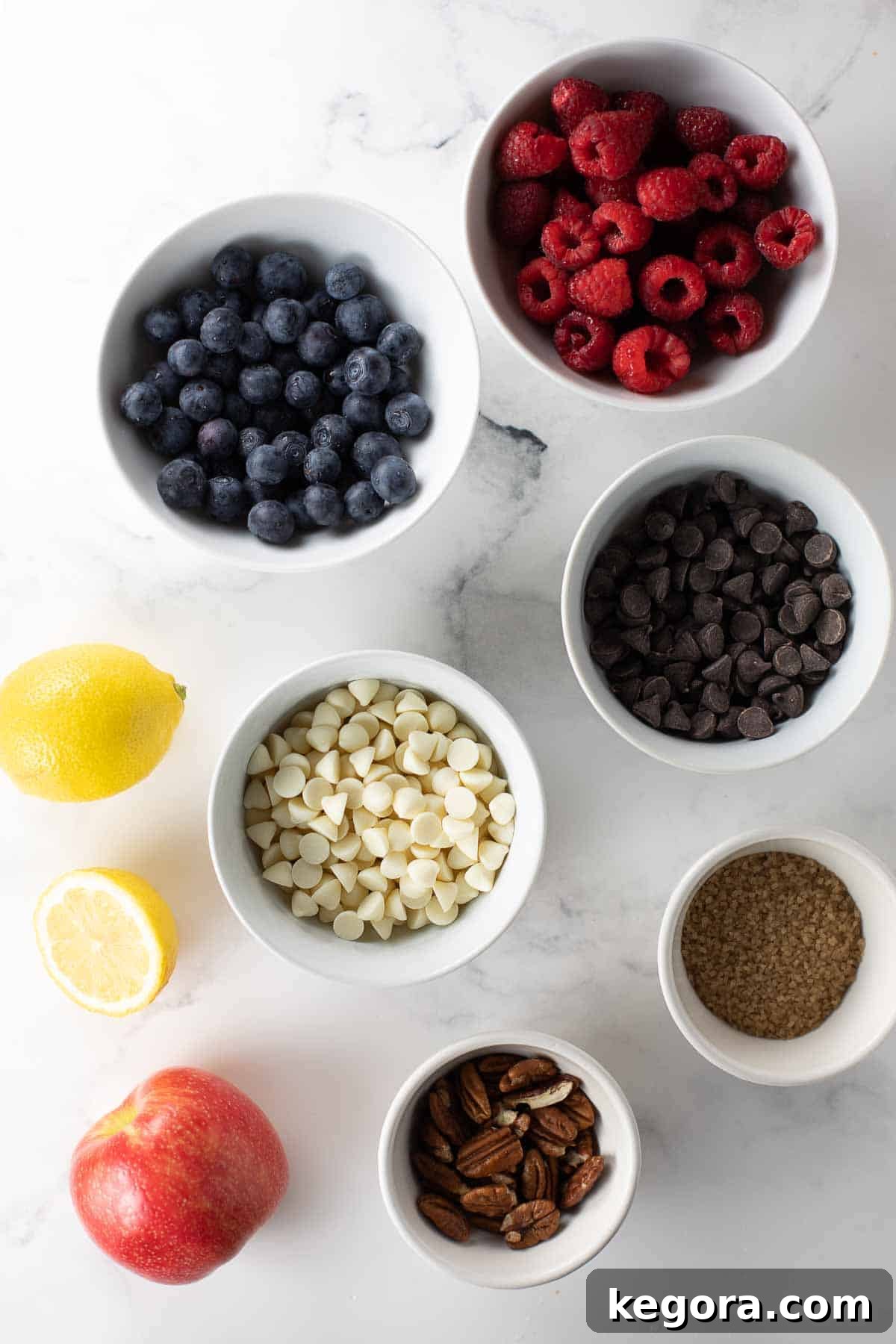 Overhead shot of various mix-ins for gluten-free muffins, including raspberries, white chocolate chips, and blueberries.