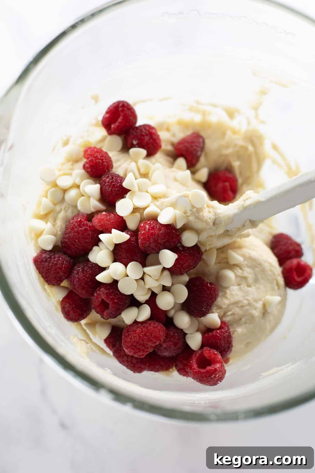Raspberries and white chocolate chips being folded into the gluten-free muffin batter.