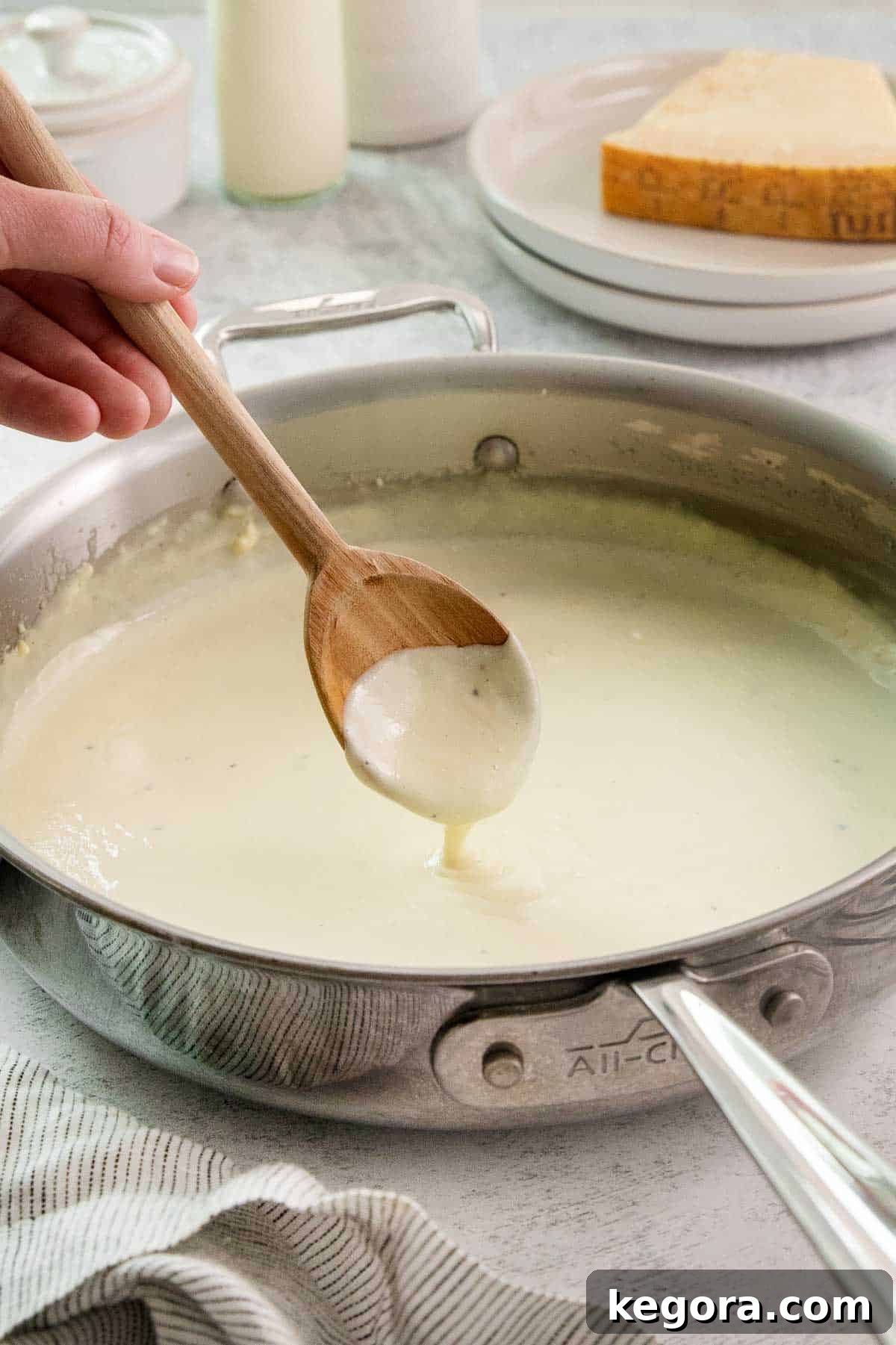Alfredo sauce in pot with sauce dripping from wooden spoon.