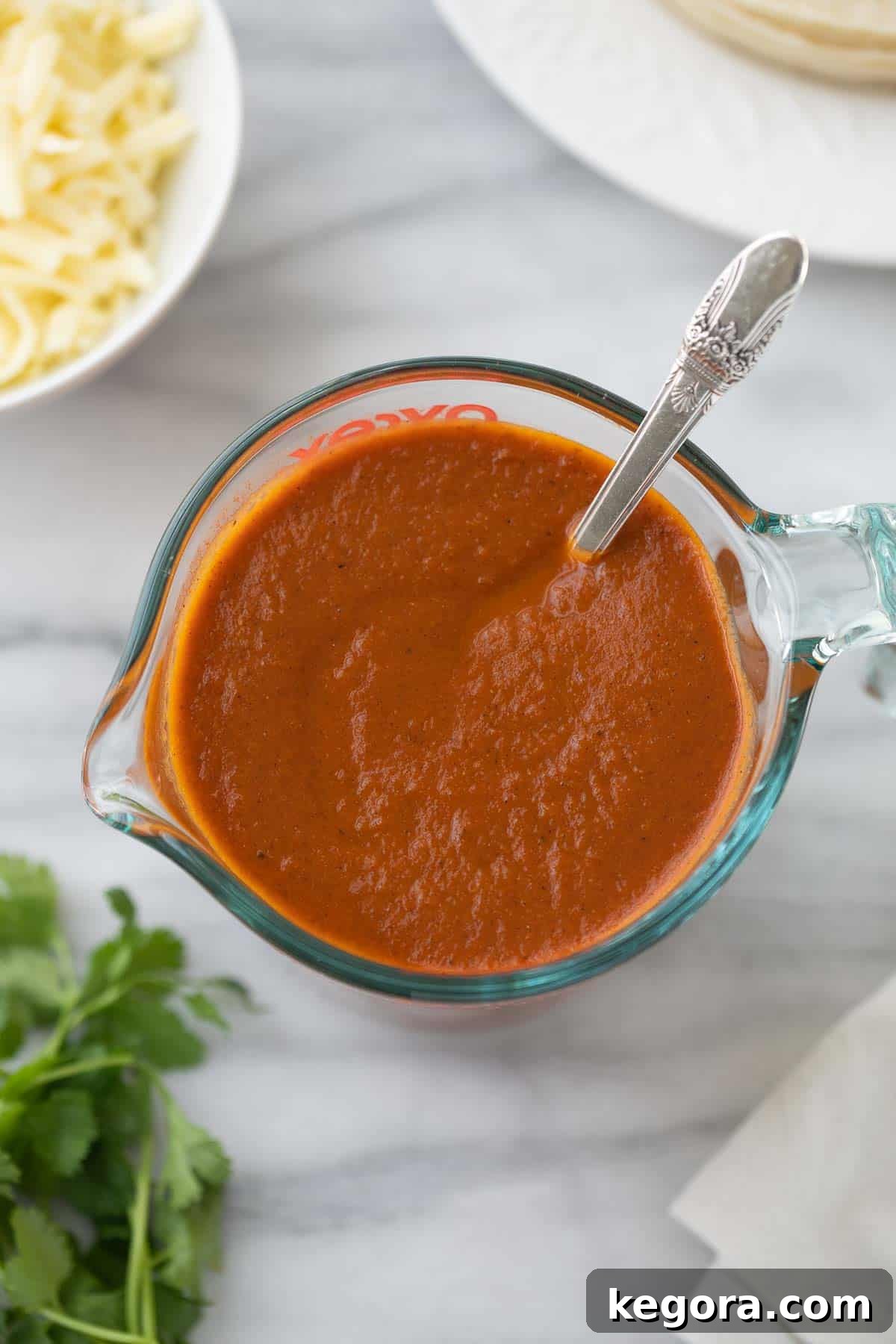A close-up shot of rich, red gluten-free enchilada sauce in a glass measuring cup, highlighting its smooth texture and inviting color.