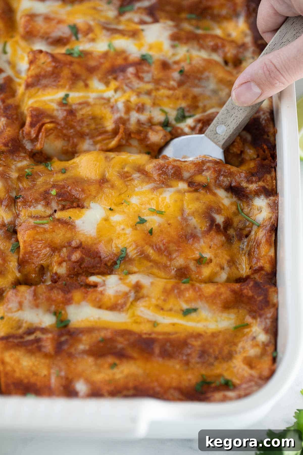 Savory Gluten Free Enchiladas 13 A spatula scooping out a generous portion of cheesy, gluten-free chicken enchiladas from a baking dish.
