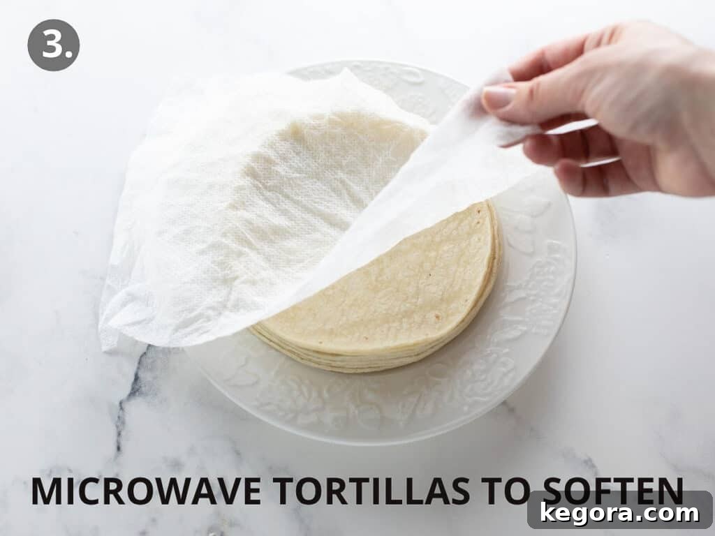Savory Gluten Free Enchiladas 7 Corn tortillas stacked on a white plate, being softened in the microwave under plastic wrap to prevent tearing during rolling.