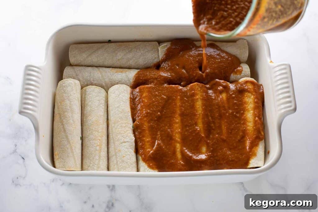 Savory Gluten Free Enchiladas 10 Rich red enchilada sauce being generously poured over the arranged gluten-free enchiladas in the baking dish.