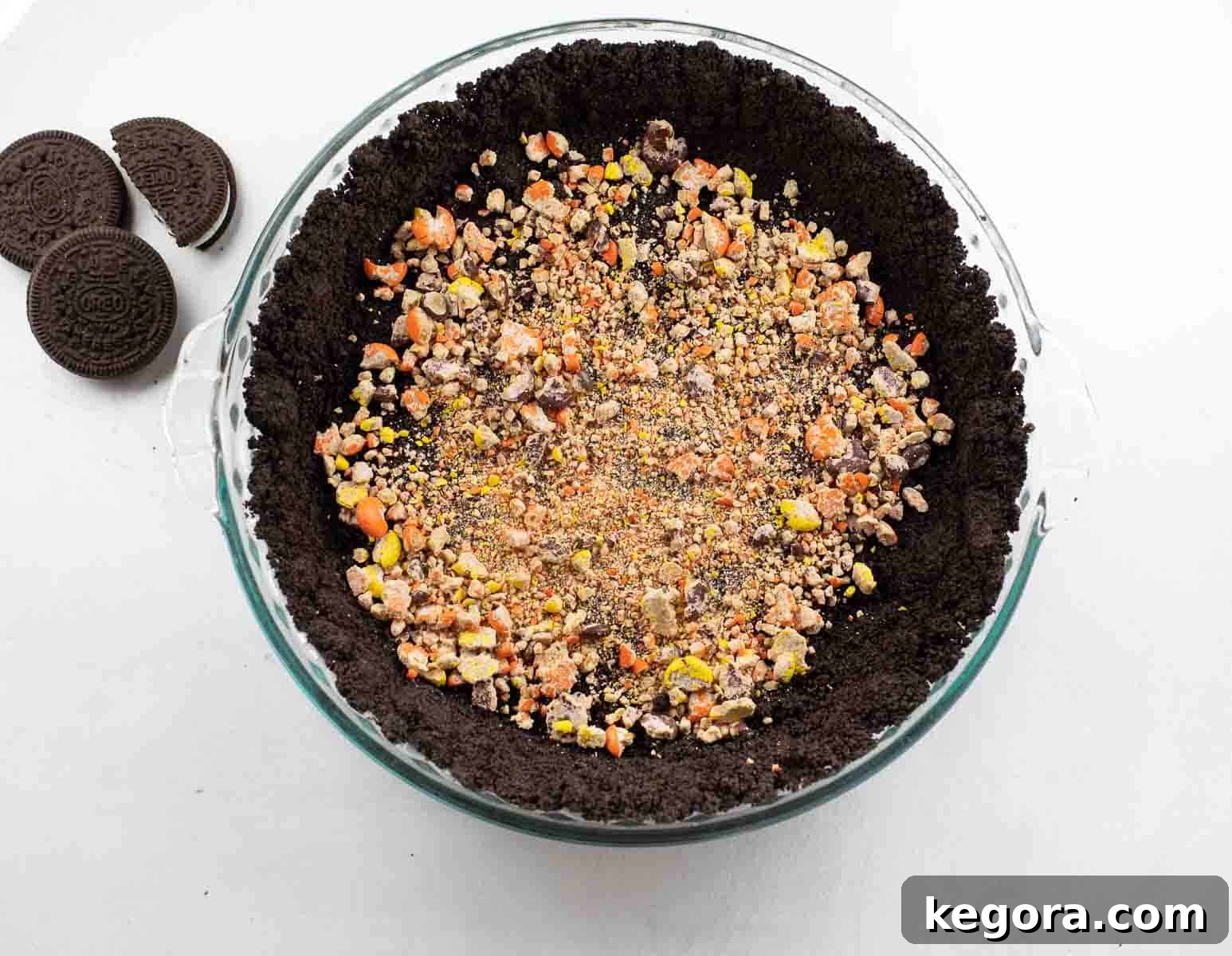 Gluten-free Oreo crust generously sprinkled with colorful Reese's Pieces candies, ready for the filling.