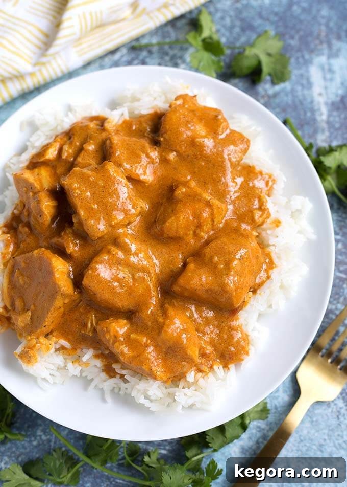 Creamy Instant Pot Butter Chicken 2 Butter Chicken over rice on white plate next to gold fork, showcasing a rich, creamy texture and succulent chicken pieces.