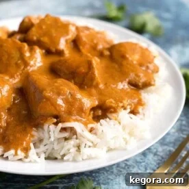 Butter Chicken over rice on white plate next to gold fork