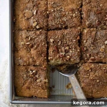 Close-up shot of a delectable gluten-free coffee cake, showcasing its moist crumb and rich cinnamon streusel topping in a metal baking dish with a piece already scooped out.