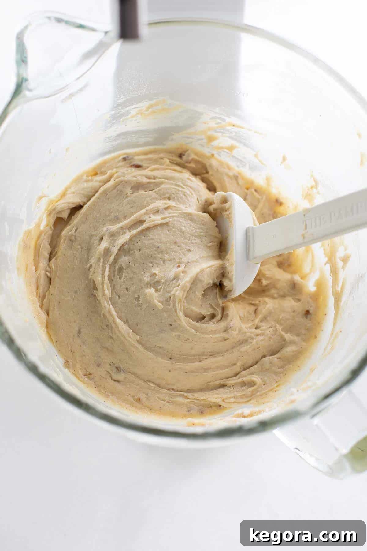 Gluten-free coffee cake batter in a clear glass bowl, with chopped nuts gently folded in, ready for layering and baking.