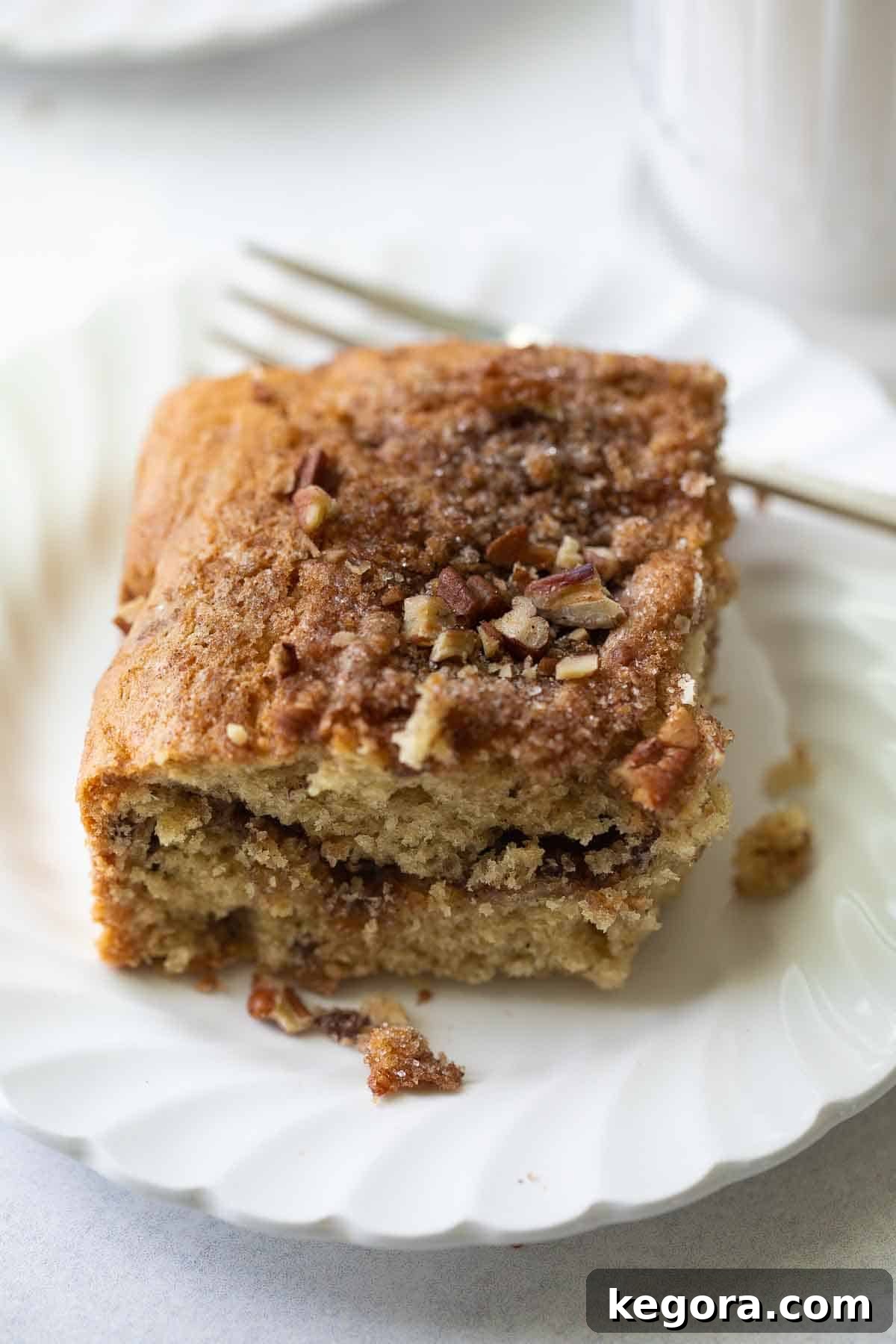 A perfectly baked slice of gluten-free coffee cake presented on a pristine white plate, accompanied by a fork, ready to be savored.