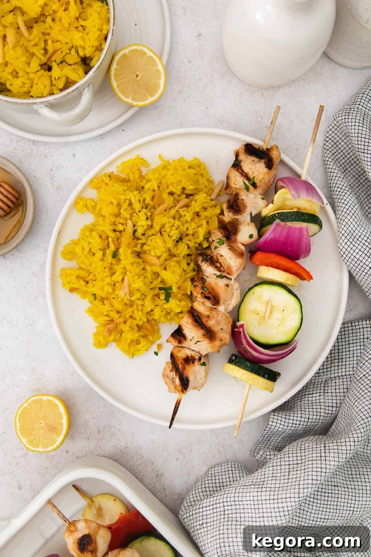 Sticky Honey Sesame Chicken Skewers Gluten and Dairy Free 6 A plate featuring a honey sesame chicken skewer and a vegetable skewer, served with fluffy yellow rice.