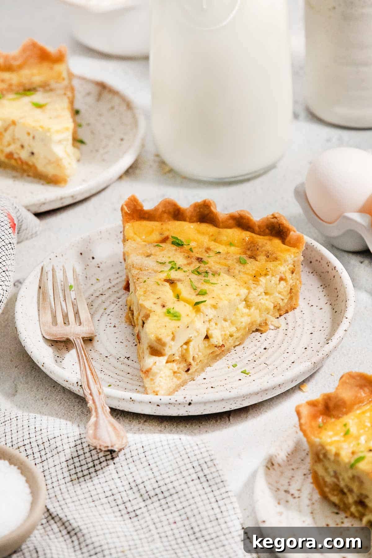 A golden-brown slice of gluten-free quiche Lorraine on a white plate, with a fork ready to enjoy.