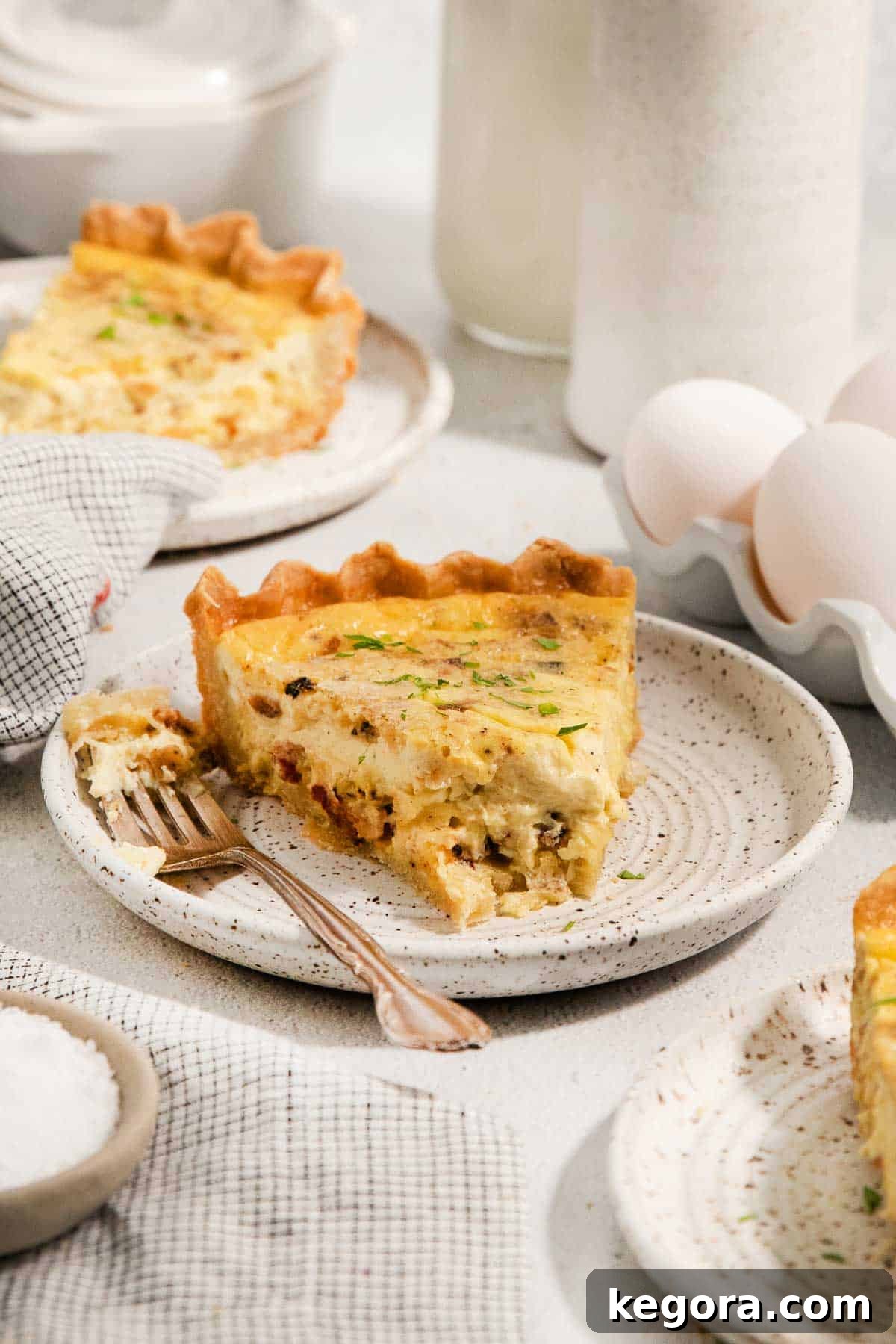 A perfect slice of gluten-free quiche Lorraine on a white plate, showcasing its flaky crust and rich filling, with a fork nearby.