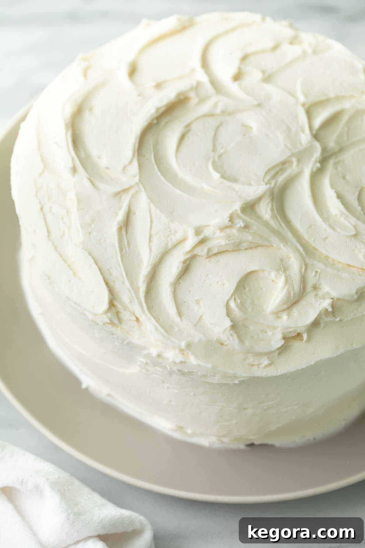 The Ultimate Gluten Free Vanilla Cake 9 A beautifully frosted gluten-free vanilla cake adorned with smooth vanilla icing, presented on a stylish gray plate.
