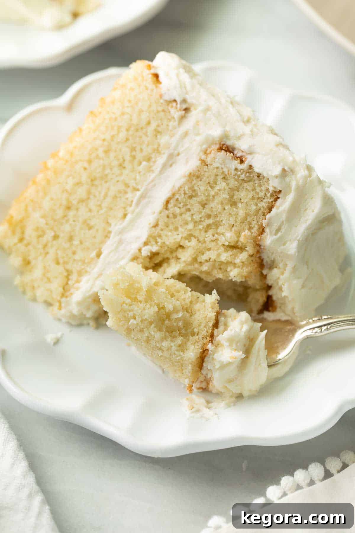 The Ultimate Gluten Free Vanilla Cake 10 A delectable slice of gluten-free cake on a white plate, with a fork about to take a bite, emphasizing its moist interior and perfect crumb.