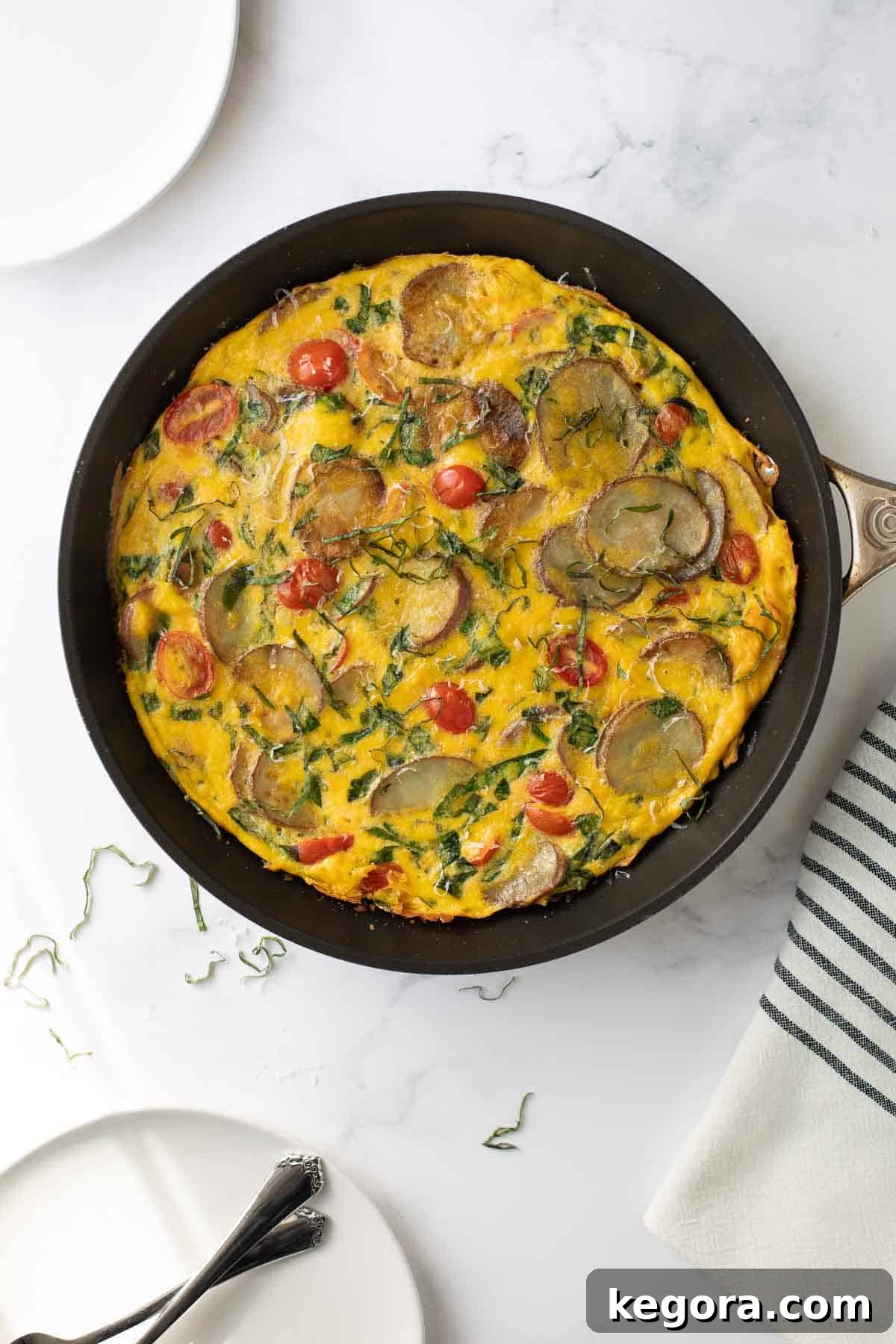 Delicious Potato Spinach Frittata Recipe Overhead view of a vibrant vegetarian frittata studded with potatoes and spinach, still in its skillet, ready to be served.