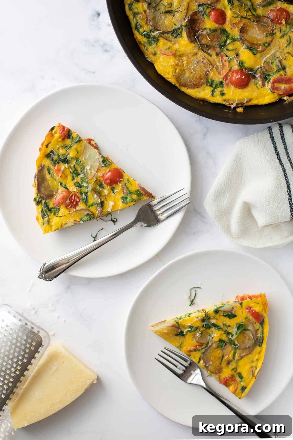 Hearty Tomato, Spinach and Potato Frittata Two plated servings of a vibrant tomato, spinach, and potato frittata, topped with melted cheese and fresh herbs, ready to be enjoyed.