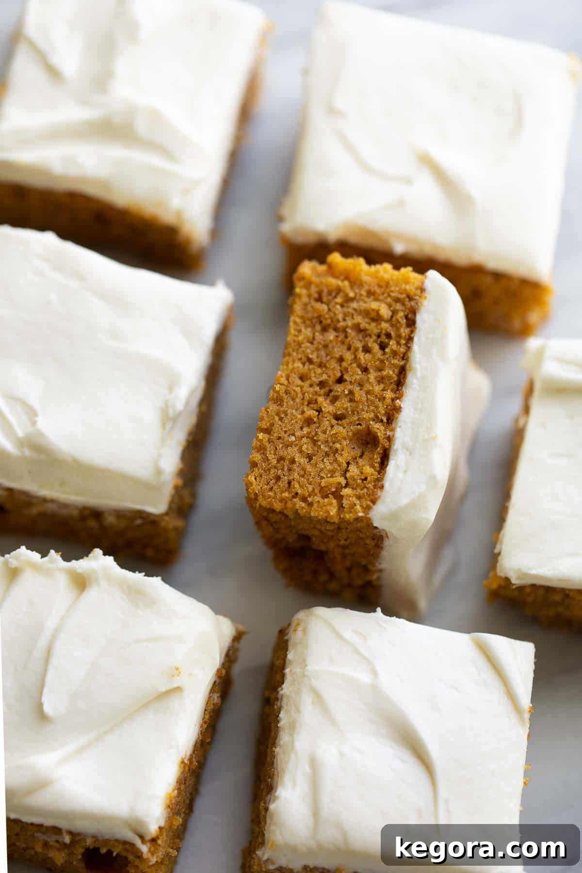 Guilt-Free Autumn Pumpkin Bars 2 Rows of gluten-free pumpkin bars with cream cheese frosting on a marble slab, ready to be served.