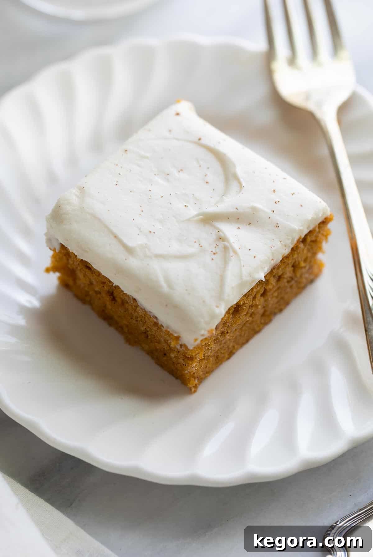 Guilt-Free Autumn Pumpkin Bars 8 A single slice of gluten-free pumpkin bar with a generous layer of cream cheese frosting, served on a white plate with a fork.