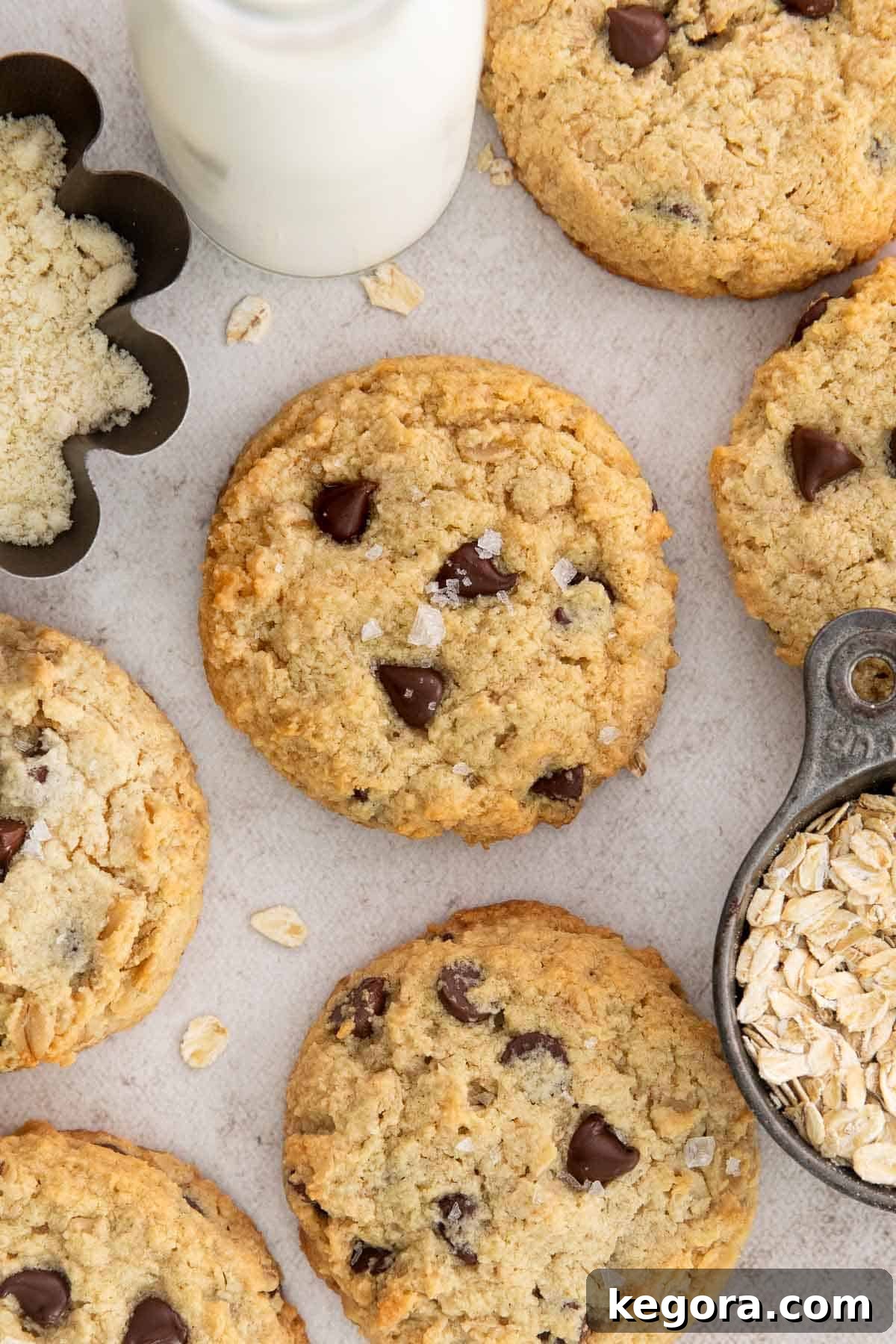 Delicious almond flour oatmeal cookies with melty chocolate chips, artfully arranged on a rustic wooden counter alongside a glass of milk and a bowl of almond flour, highlighting their wholesome appeal.