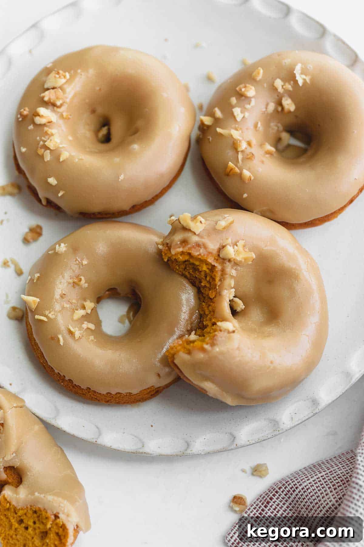 Gluten-free pumpkin donuts on a white plate topped with chopped walnuts, a perfect fall treat.