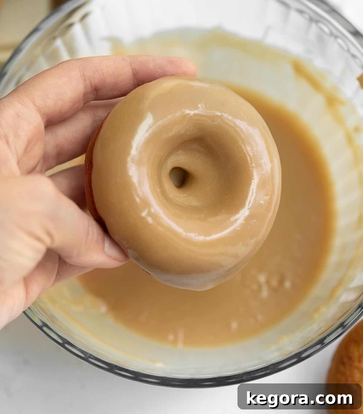 A gluten-free donut being dipped into a luscious brown sugar glaze, showing the process of adding the final touch.