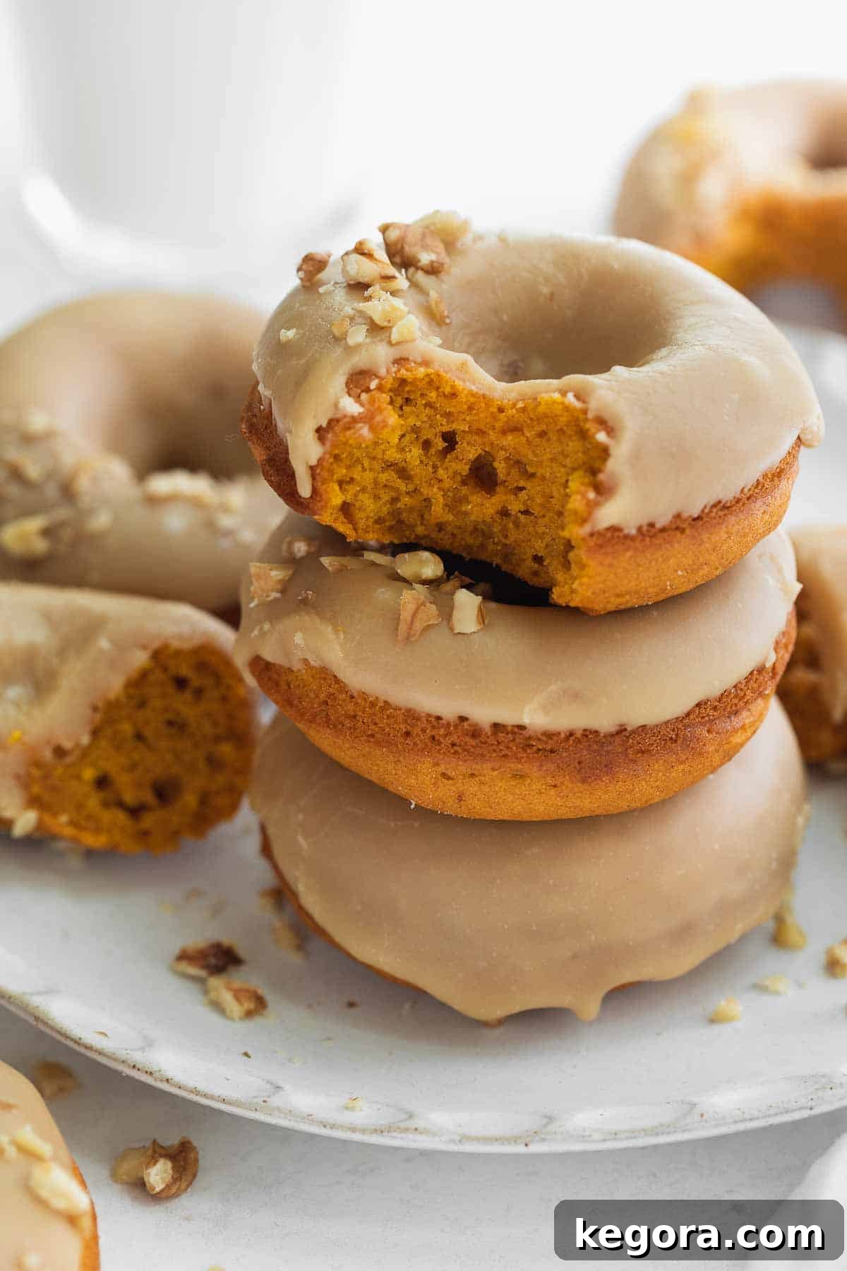 Gluten-free pumpkin donuts stacked on a white plate, with one having a bite taken out, highlighting its fluffy texture.