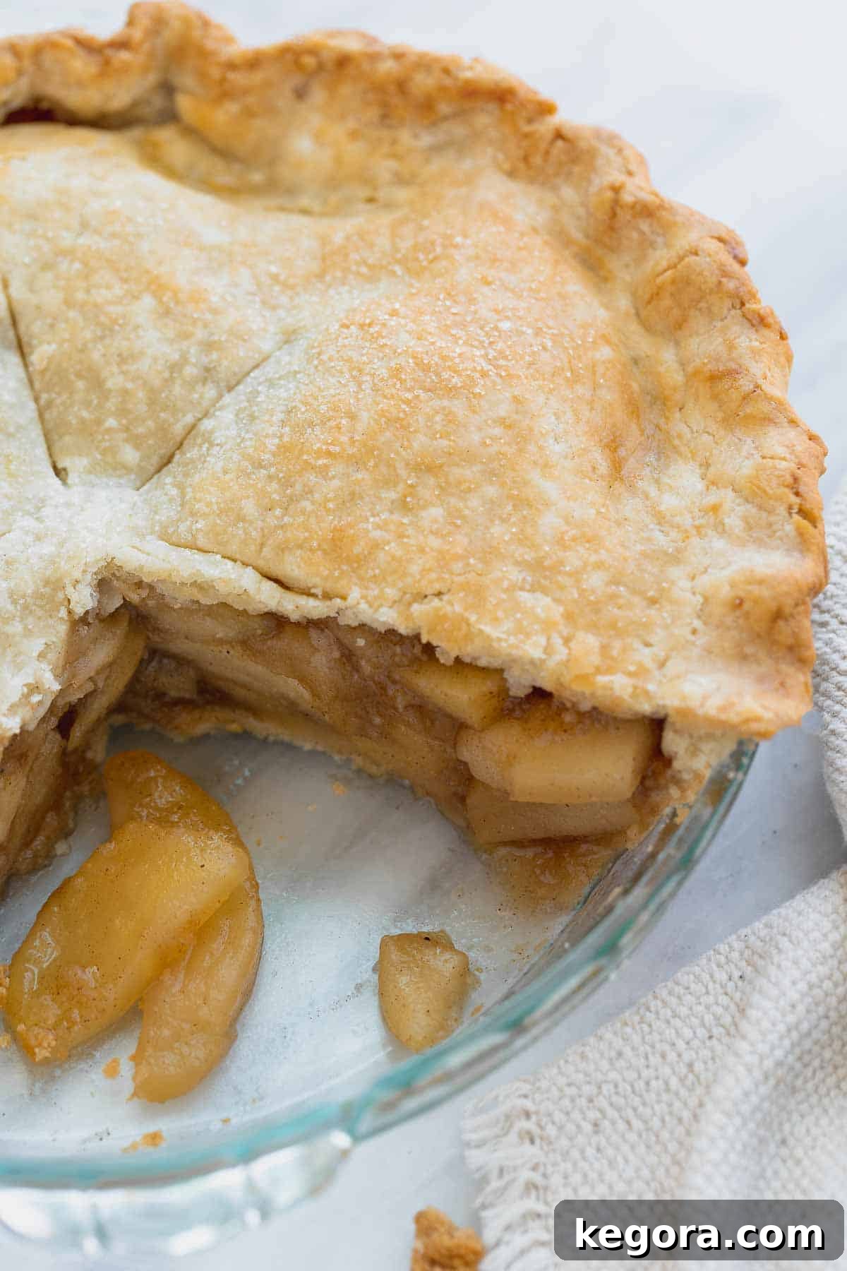 Close-up of a golden brown gluten-free apple pie in a pan with a slice cut out, revealing the apple filling.