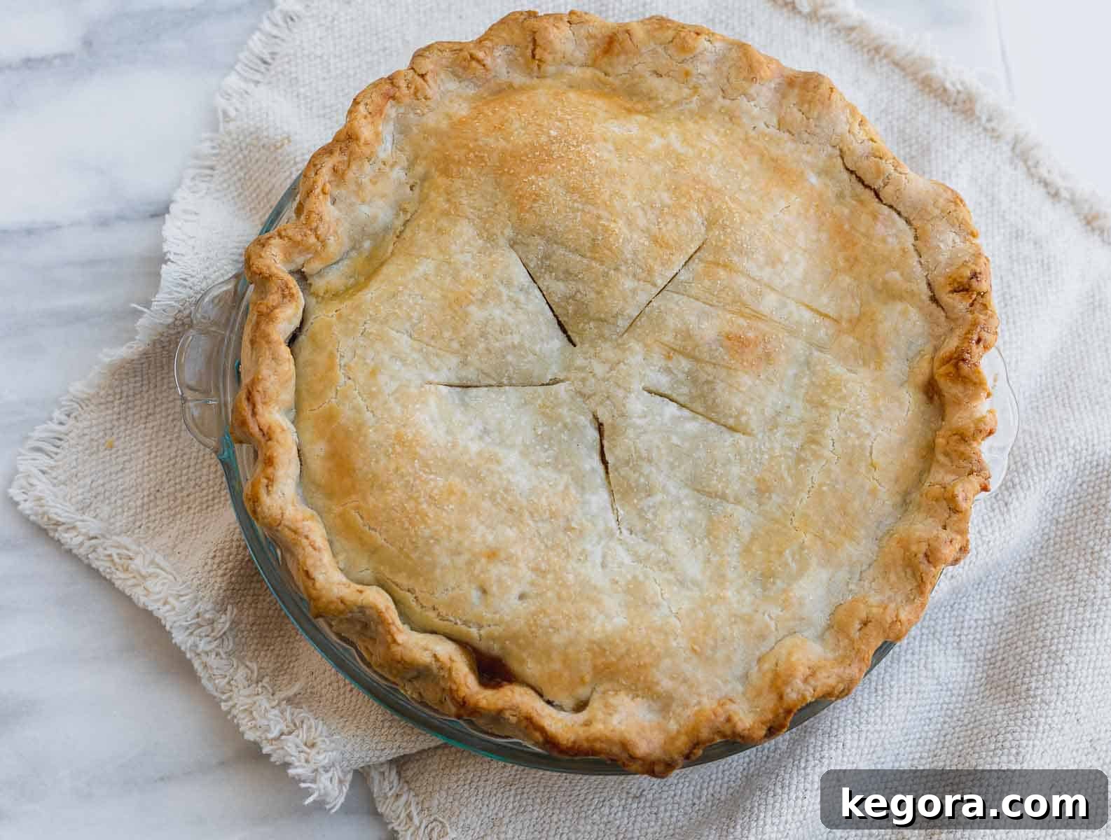 Gluten-free apple pie cooling on a brown dish towel after baking.