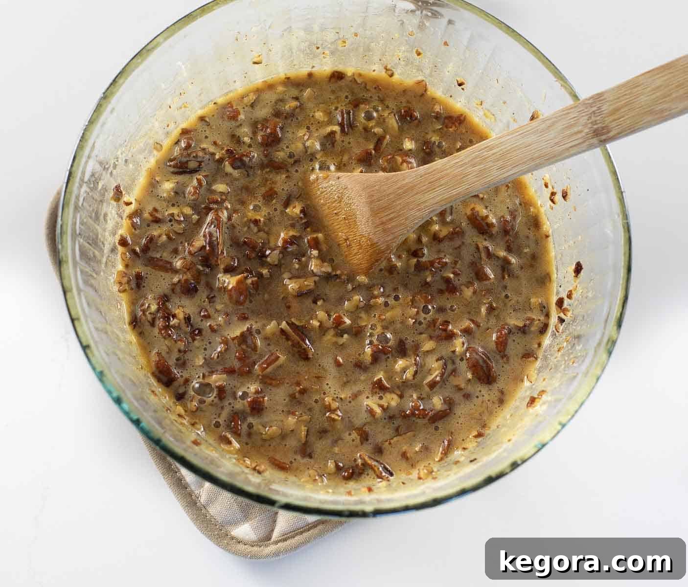 Decadent Gluten-Free Pecan Pie 10 pecan pie filling in glass bowl being stirred with wooden spoon