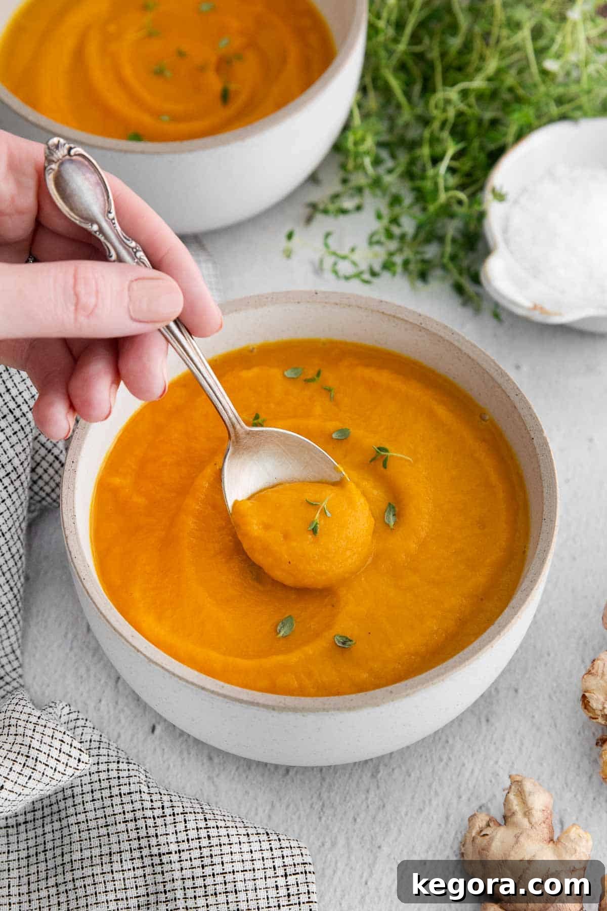 A bowl of vibrant carrot ginger soup with a spoonful being scooped, showcasing its creamy texture.