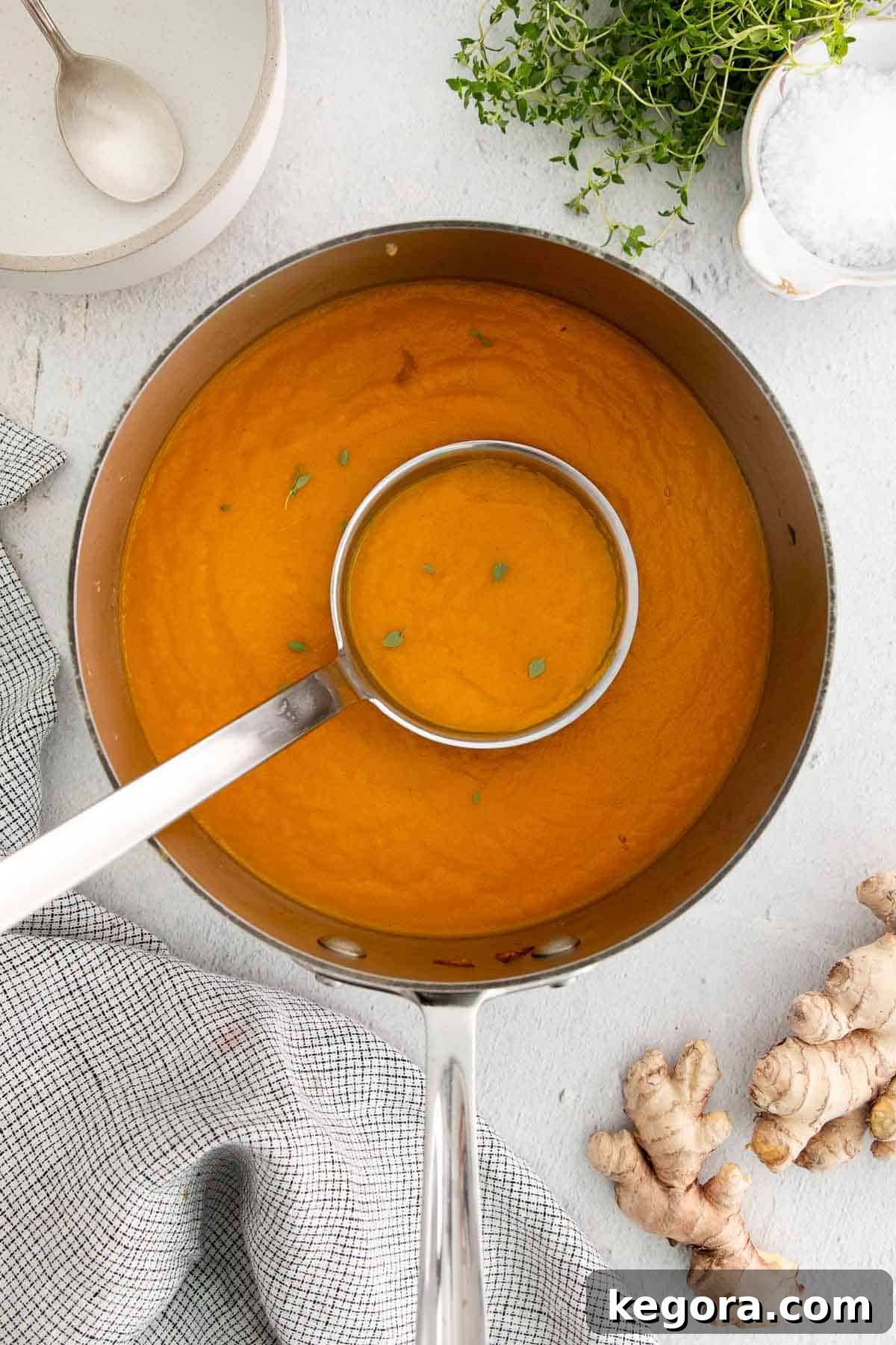 A large pot of creamy carrot ginger soup with a ladle scooping some up, ready to serve.