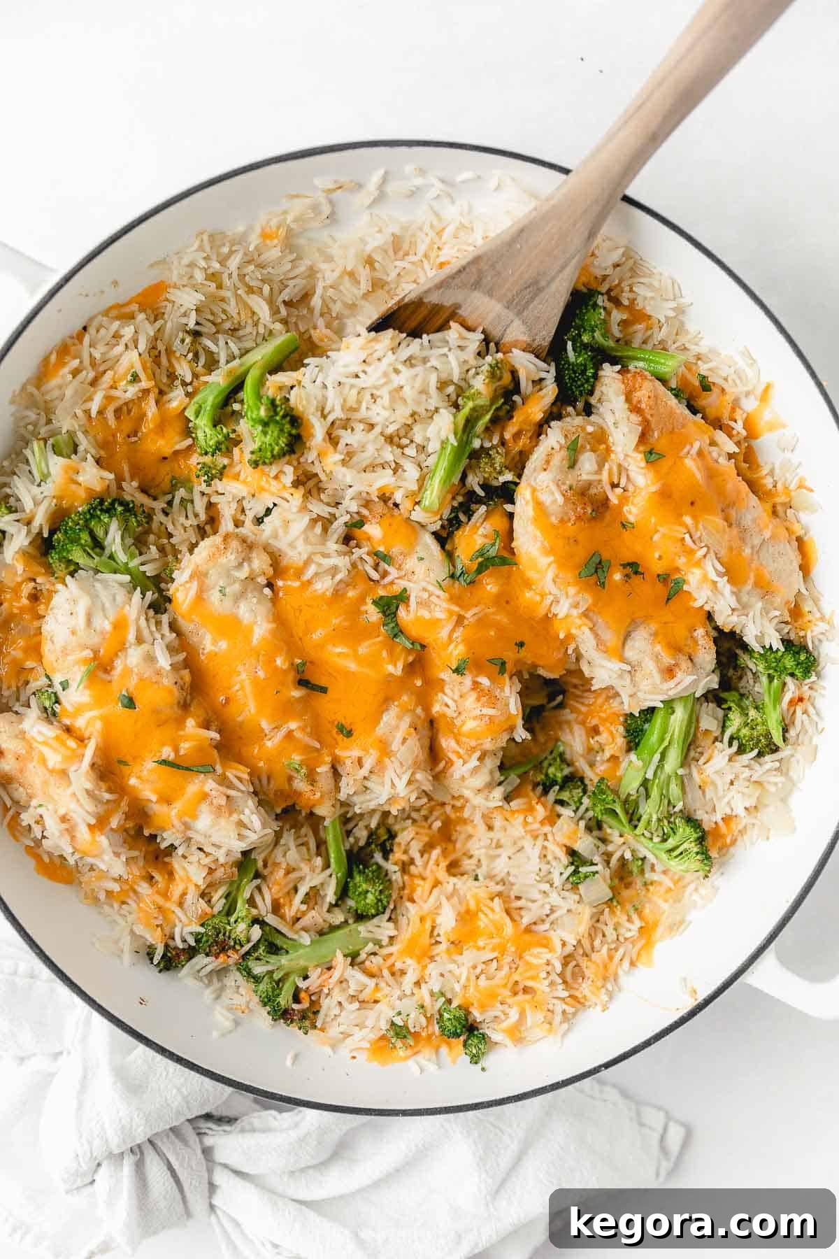 Overhead shot of the finished gluten-free chicken and broccoli cheddar rice dish in a white serving dish, with a wooden spoon scooping a portion.
