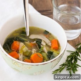 A hearty bowl of chicken soup with vegetables, a spoon, and a glass of water on the side.