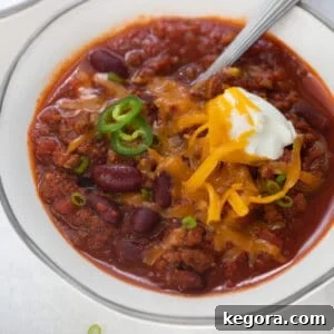 Award-winning gluten-free chili in a white bowl, generously topped with sour cream and shredded cheese.
