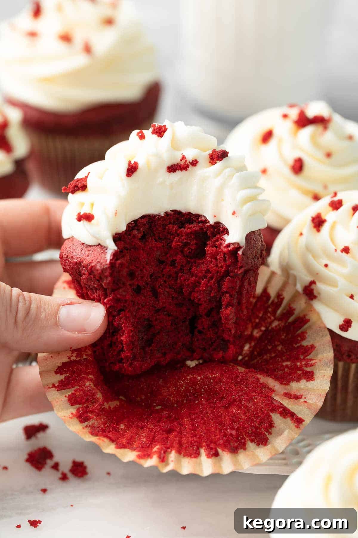 Close-up shot of a single gluten-free red velvet cupcake with swirled cream cheese frosting, on a white plate.