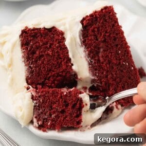 A fork taking a delicious bite out of a perfectly frosted slice of gluten-free red velvet cake.