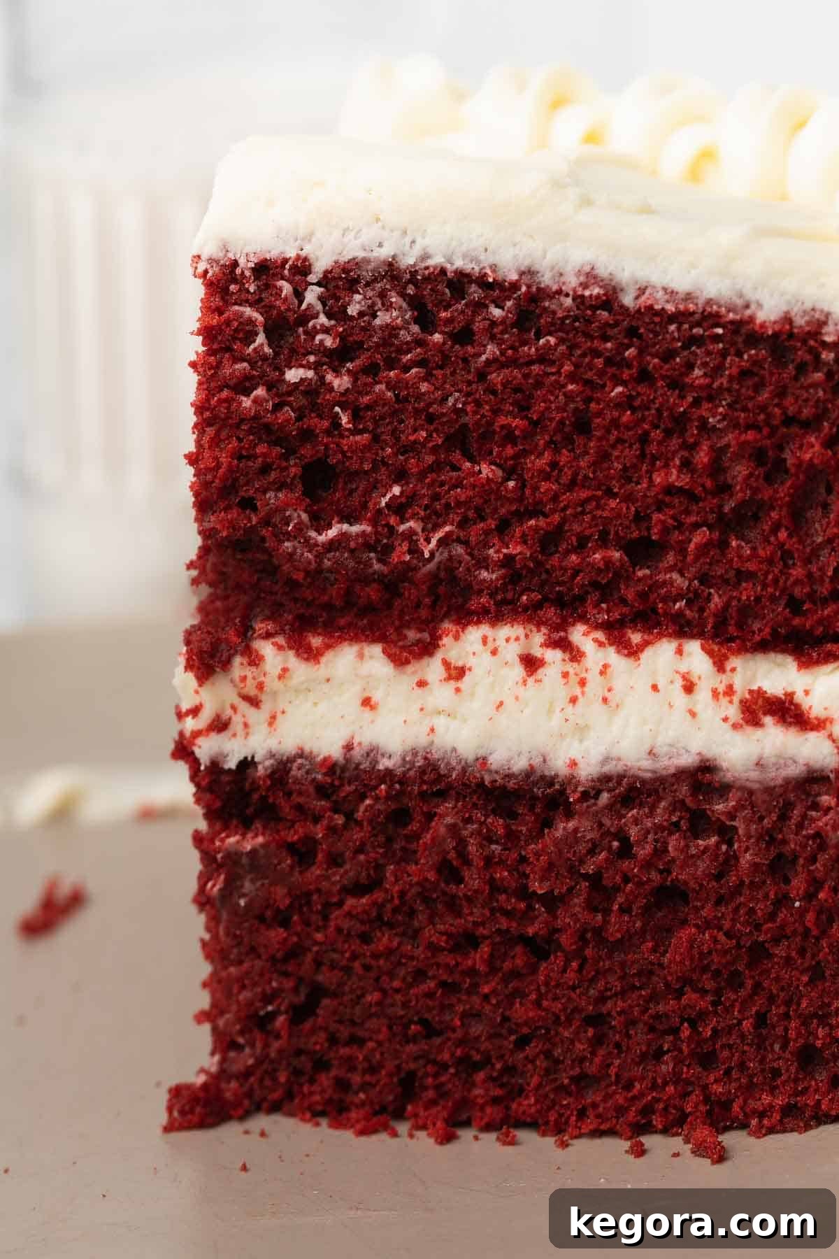A perfectly sliced piece of gluten-free red velvet cake, showcasing its vibrant red layers and luscious cream cheese frosting, resting on a gray plate.