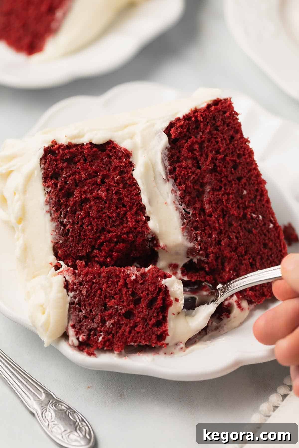 A fork poised to take a delicious bite out of a gluten-free red velvet cake slice, showing its moist crumb and rich frosting.