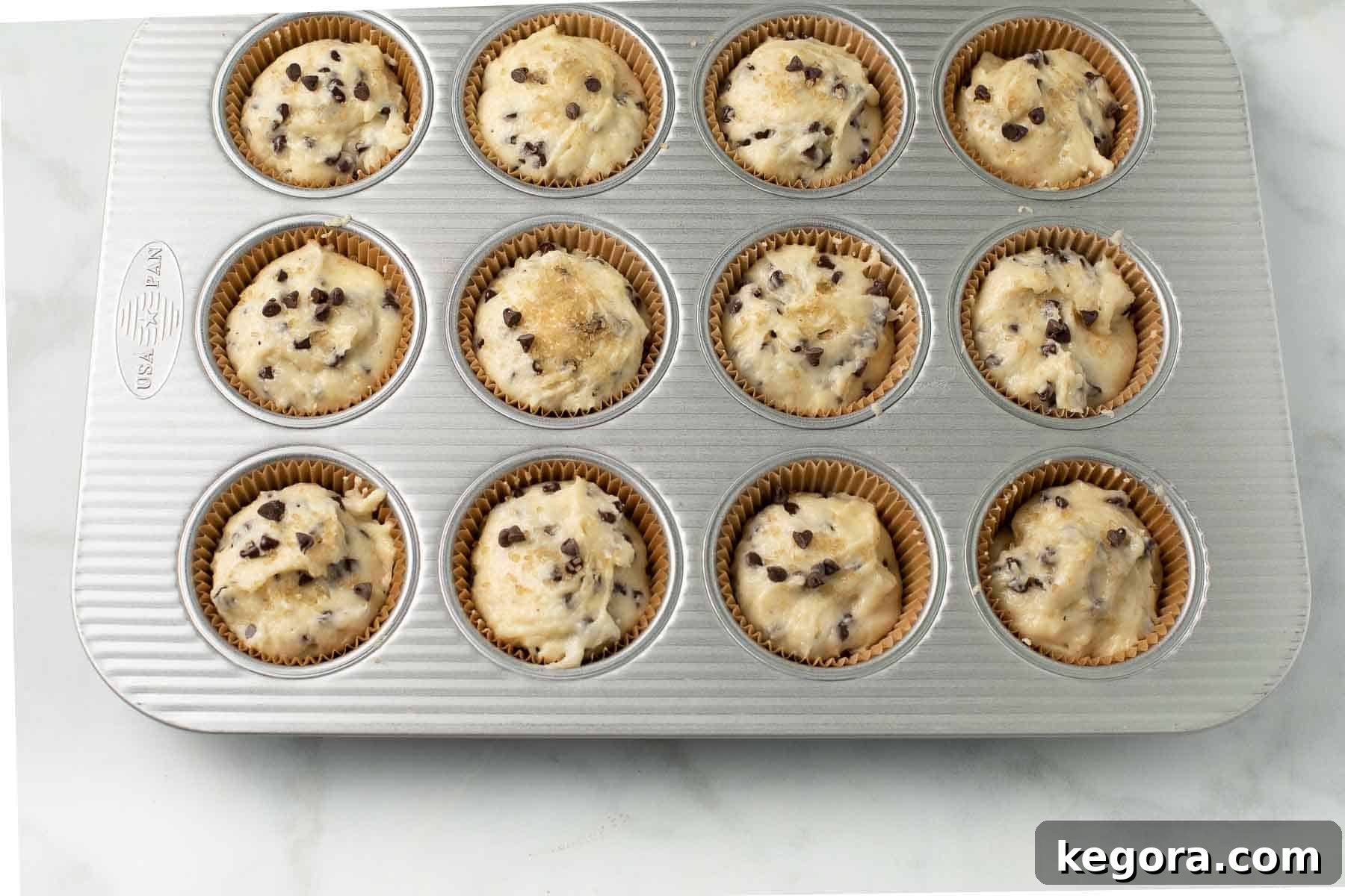 Decadent Gluten-Free Chocolate Chip Muffins 7 Muffin batter neatly portioned into paper liners in a muffin tin, sprinkled with raw sugar, and ready for baking into gluten-free chocolate chip muffins.