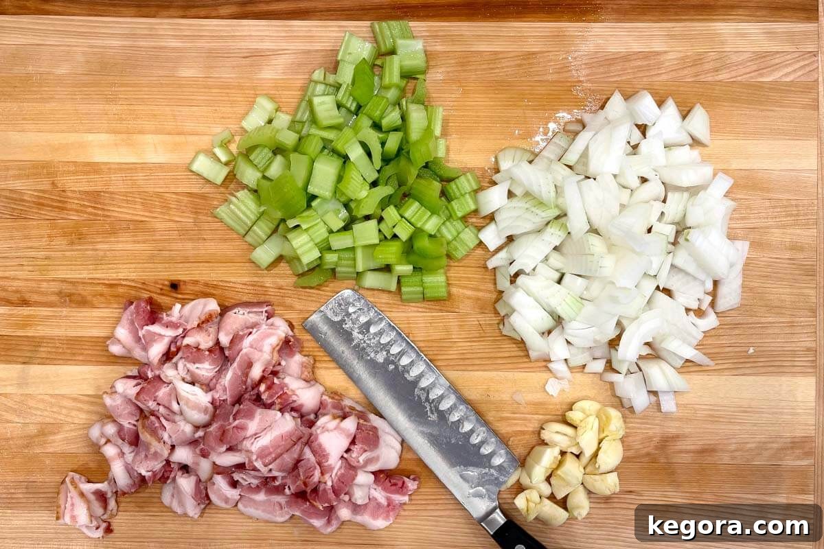 bacon, celery, onion, garlic chopped on board with knife.