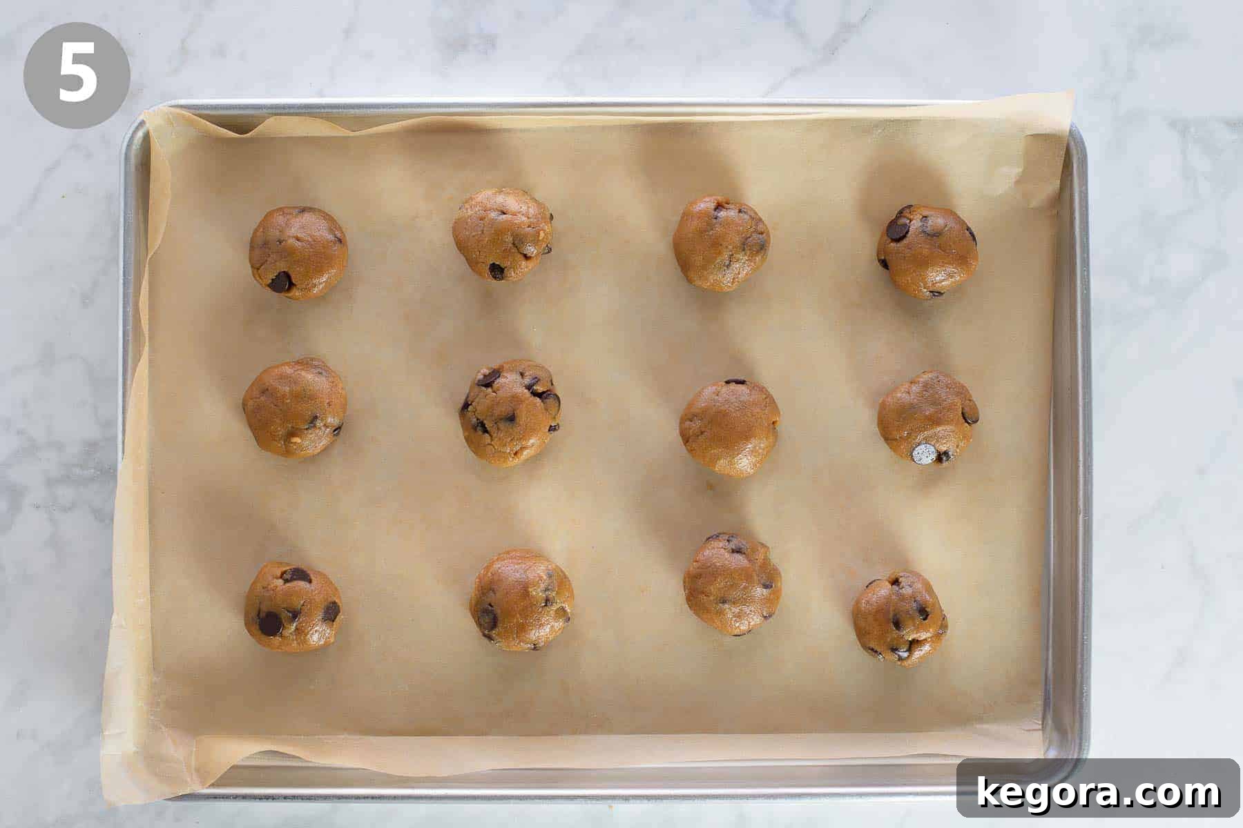 Close-up shot of perfectly formed cookie dough balls arranged on a parchment paper-lined baking sheet, evenly spaced and ready to be baked into delicious flourless peanut butter chocolate chip cookies.
