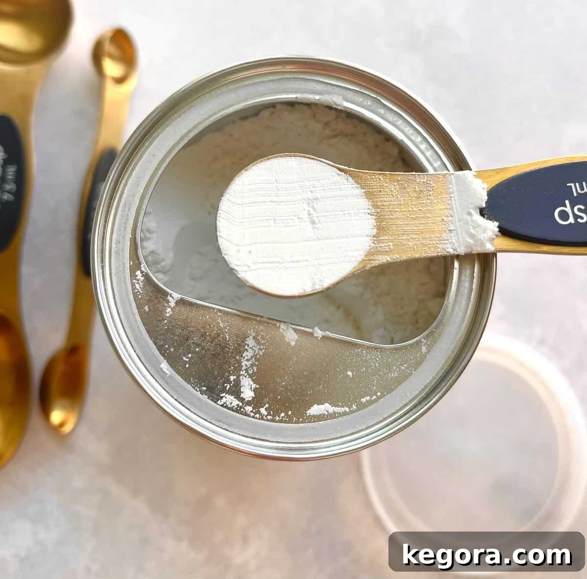 A measuring spoon full of white baking powder being scooped from a container.