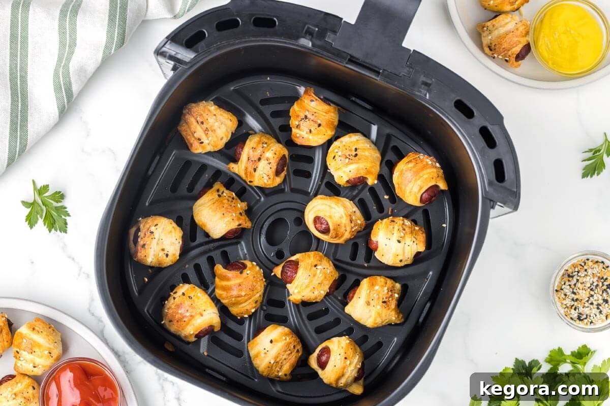 A basket full of freshly cooked, golden brown Air Fryer Pigs in a Blanket, ready to be removed.