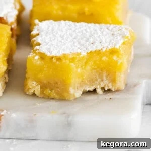 A tantalizing close-up of a perfectly golden gluten-free lemon bar with a bite taken out, revealing its thick, zesty lemon filling and buttery shortbread crust.
