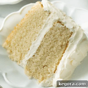 A perfect slice of light, fluffy gluten-free vanilla cake, elegantly frosted with creamy vanilla buttercream, resting on a white plate, symbolizing pure celebration.